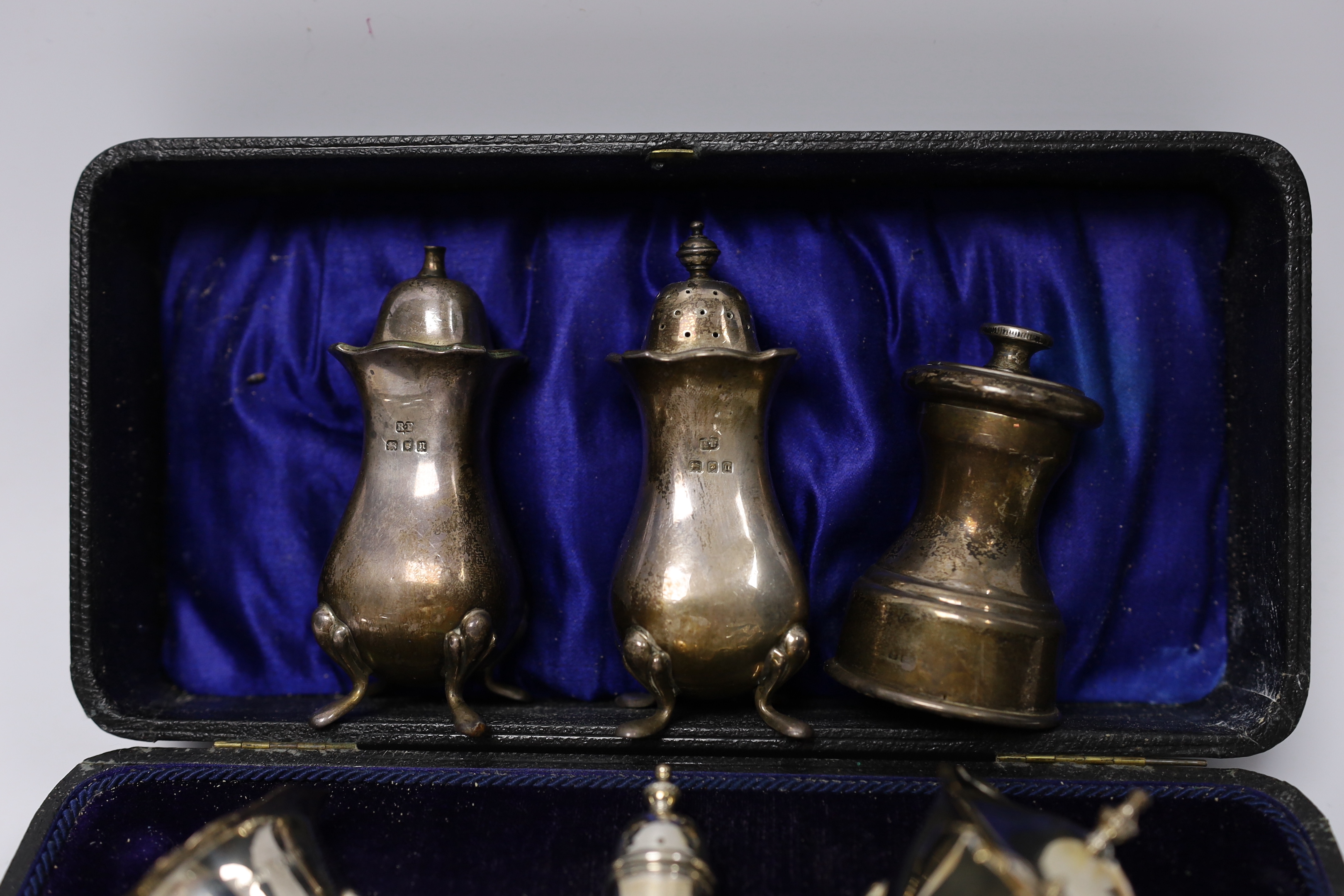 A cased George V silver three piece condiment set, Birmingham, 1919, a pair of later silver pepperettes and a silver mounted pepper mill.